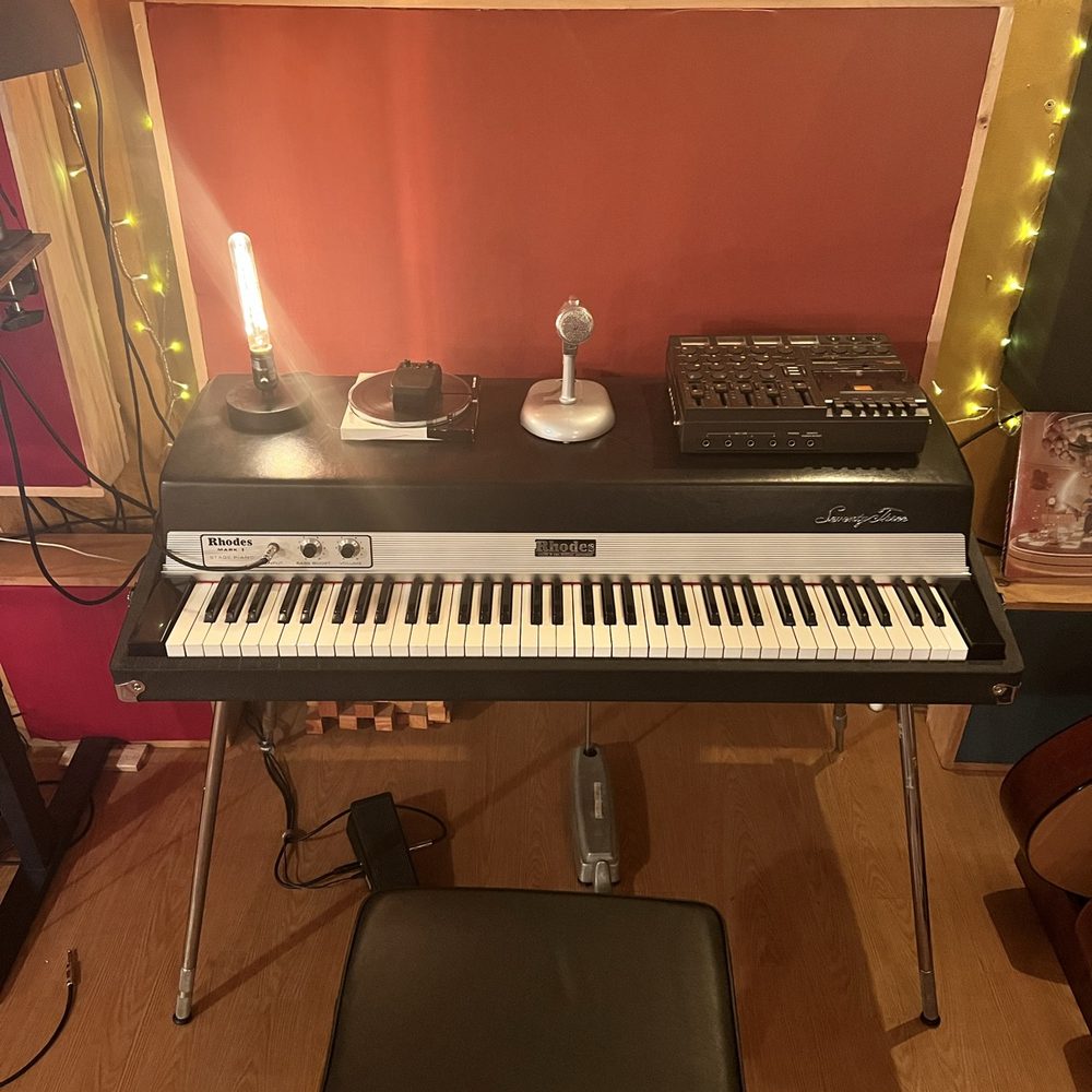 A vintage Rhodes Mark I Seventy Three electric piano lit by an Edison bulb against a deep red studio wall